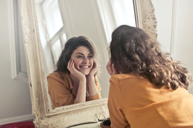 Woman wearing a yellow t-shirt looking at a mirror and smiling